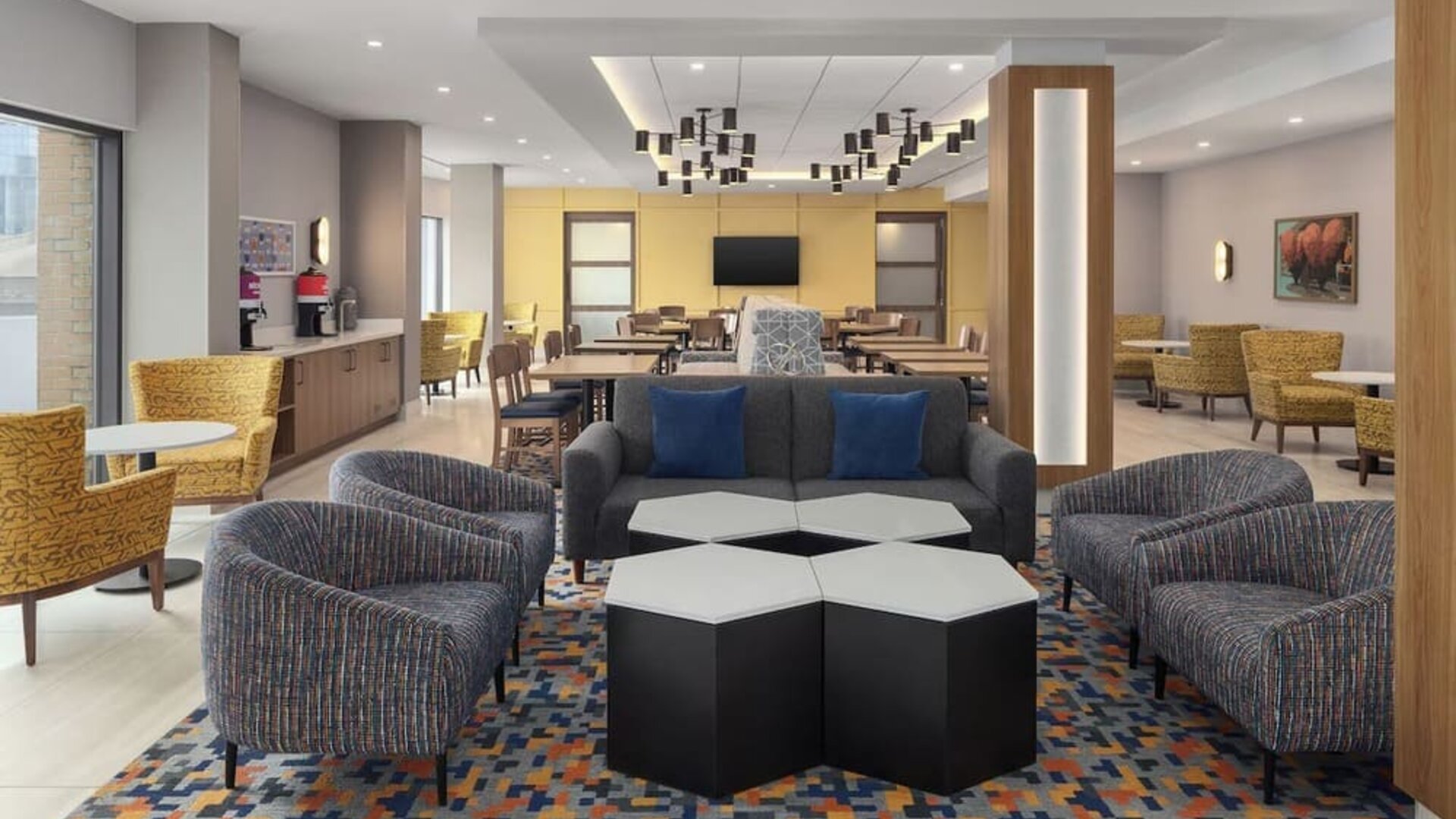 Modern hotel lobby with lounge seating, coffee station, dining area, and geometric patterned carpet at Hampton Inn By Hilton Montreal East Anjou.