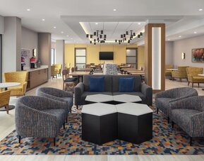 Modern hotel lobby with lounge seating, coffee station, dining area, and geometric patterned carpet at Hampton Inn By Hilton Montreal East Anjou.