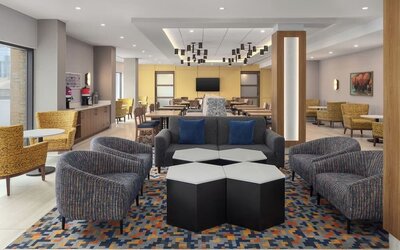 Modern hotel lobby with lounge seating, coffee station, dining area, and geometric patterned carpet at Hampton Inn By Hilton Montreal East Anjou.
