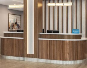 Reception desk with wood paneling, Hilton Honors signage, and contemporary lighting at Hampton Inn By Hilton Montreal East Anjou.