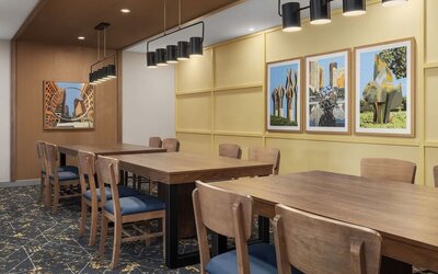 Dining area with communal tables, framed artwork, and modern pendant lighting at Hampton Inn By Hilton Montreal East Anjou.