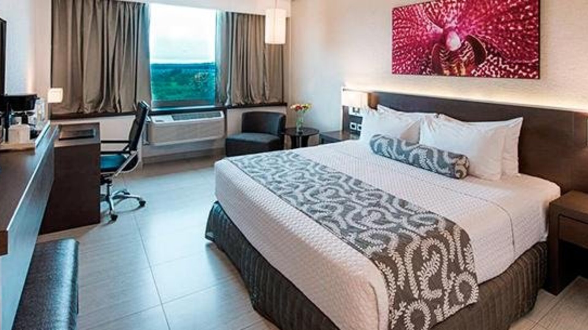 Contemporary king guest room with a large bed, dedicated workspace, flat-screen television, and large windows providing natural light at Crowne Plaza Panama Airport.