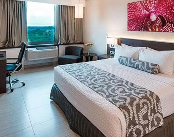 Contemporary king guest room with a large bed, dedicated workspace, flat-screen television, and large windows providing natural light at Crowne Plaza Panama Airport.