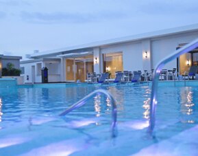 Outdoor swimming pool area at Crowne Plaza Panama Airport with spacious lounging areas and evening lighting, offering a relaxing environment for guests.