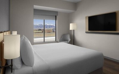 King guest room with mountain views, lounge chair, and wall-mounted television at Hyatt Place Bozeman Yellowstone Airport.