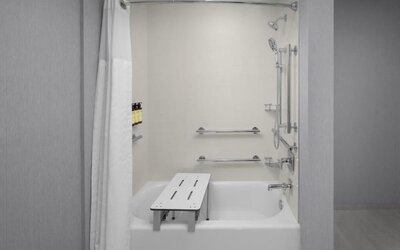 Accessible bathroom with bathtub, grab bars, handheld showerhead, and transfer bench at Hyatt Place Bozeman Yellowstone Airport.