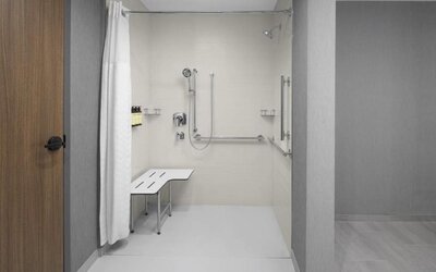Accessible roll-in shower with grab bars, handheld showerhead, and built-in transfer bench at Hyatt Place Bozeman Yellowstone Airport.