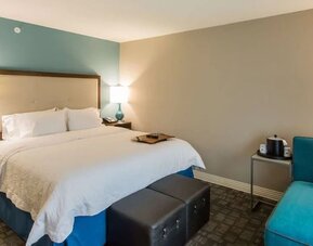 King guest room with comfortable bed, lounge chair, and contemporary décor at Hampton Inn & Suites Orlando at SeaWorld.