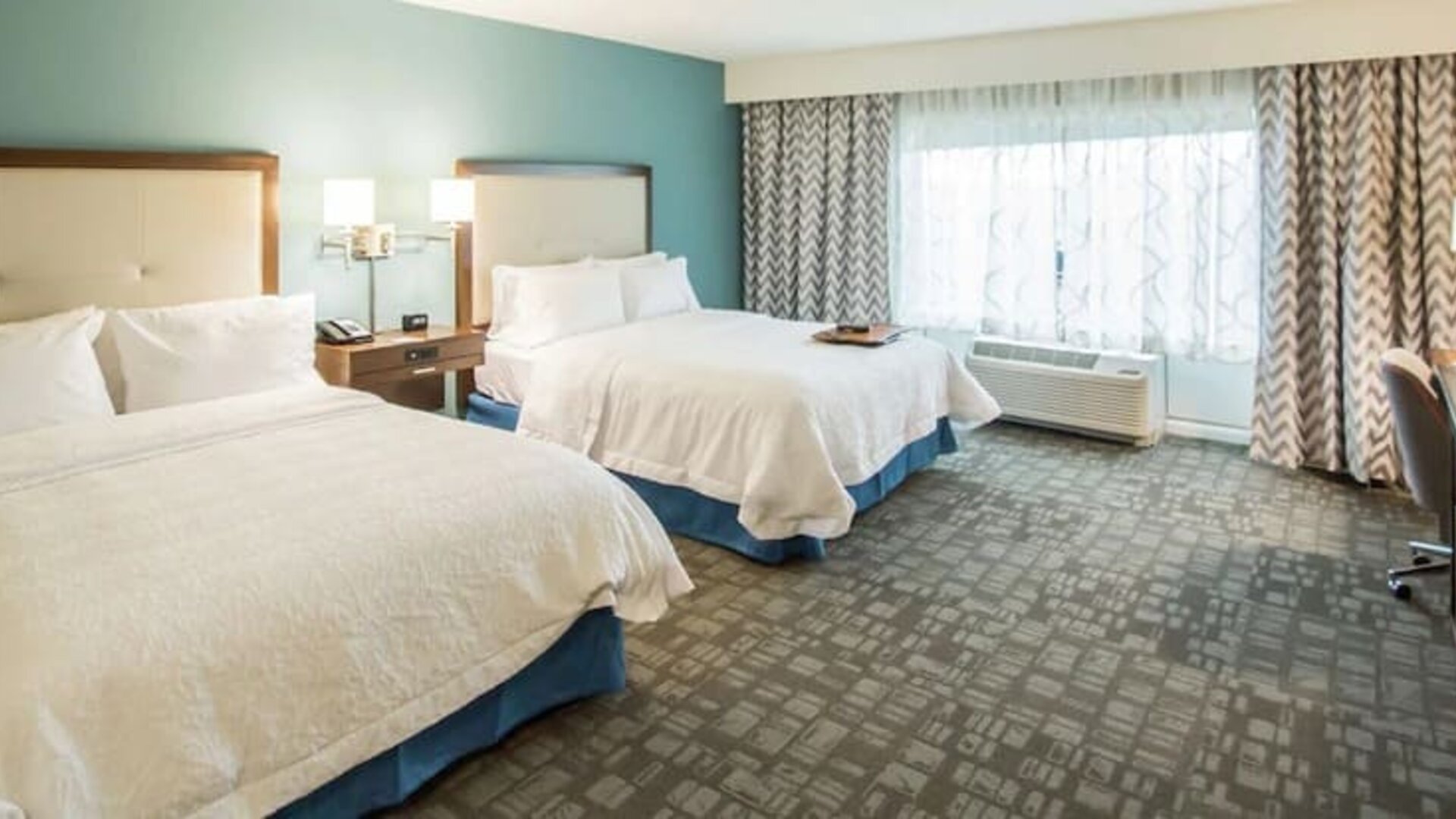 Spacious guest room with two queen beds, work desk, and large window at Hampton Inn & Suites Orlando at SeaWorld.