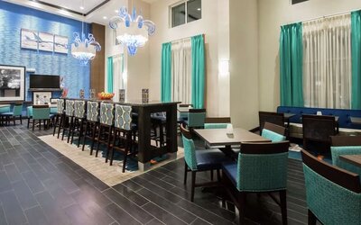 Bright dining area with communal seating, high-top tables, and contemporary décor at Hampton Inn & Suites Orlando at SeaWorld.