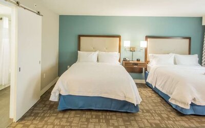 Guest room with two queen beds, spacious layout, and accessible bathroom entrance at Hampton Inn & Suites Orlando at SeaWorld.