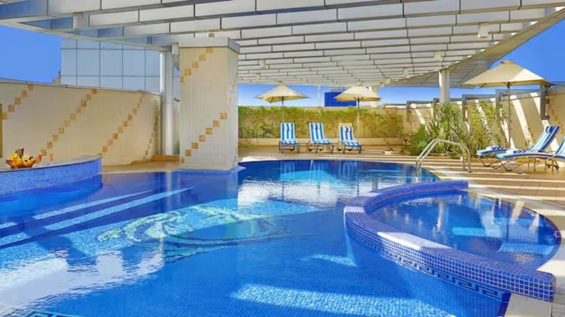 Covered outdoor pool with curved design, lounge chairs, shaded seating areas, and relaxing leisure space.