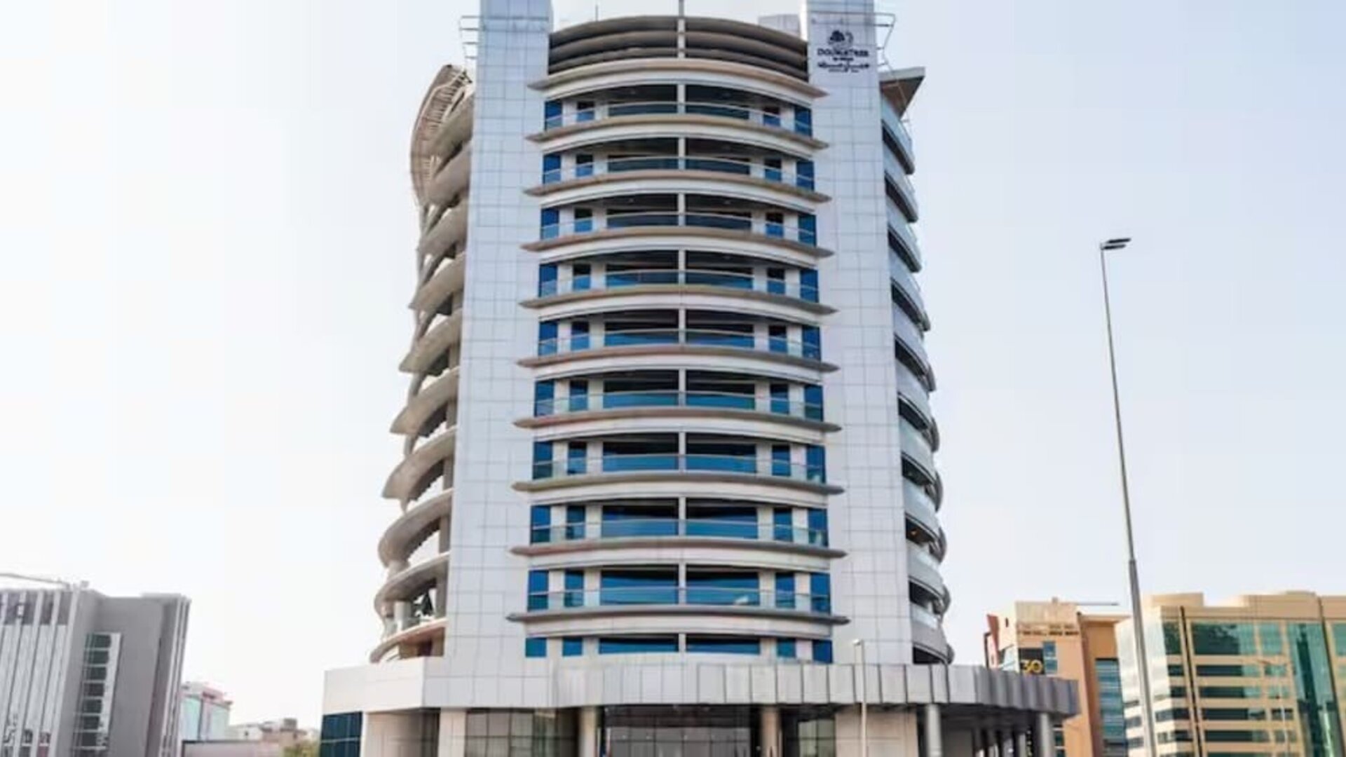 Contemporary high-rise hotel building with curved architectural design, glass windows, and city surroundings.