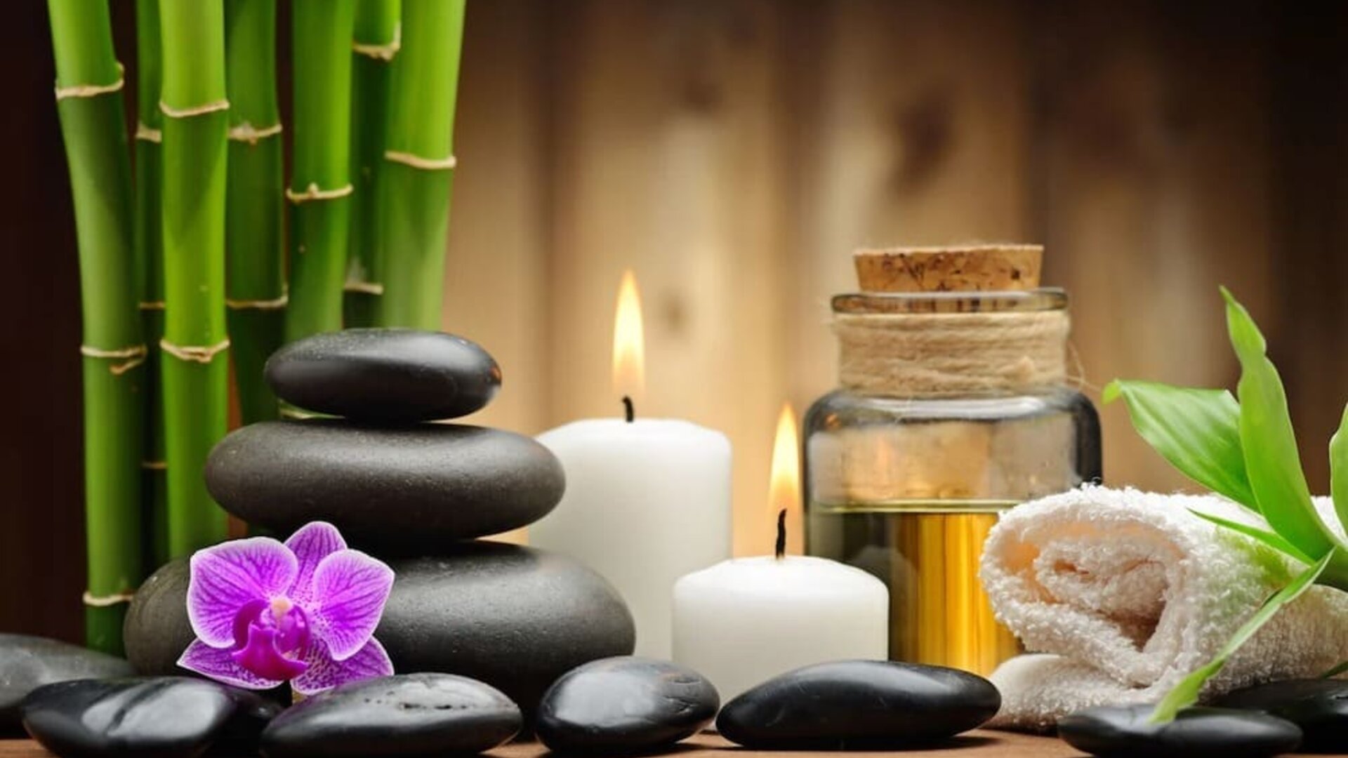 Spa-inspired arrangement with bamboo, smooth stones, candles, orchid flower, essential oil, and rolled towel.