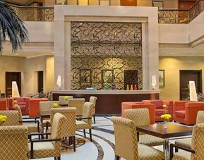 Elegant hotel lobby with comfortable seating, decorative wall feature, indoor palm accents, and welcoming atmosphere.