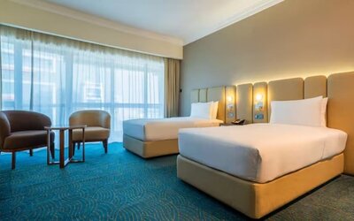 Comfortable twin-bed room with upholstered headboards, sitting area, floor-to-ceiling curtains, and soft ambient lighting.