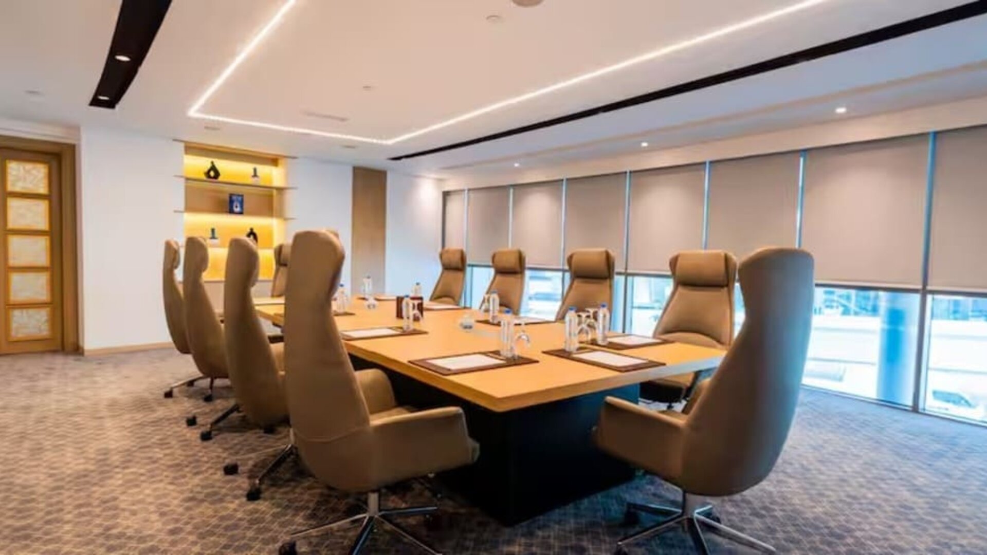 Professional boardroom with executive chairs, large conference table, floor-to-ceiling windows, and modern lighting.