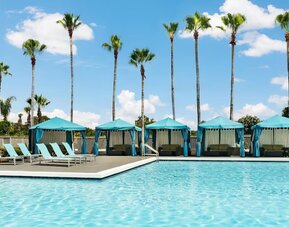 Outdoor swimming pool with turquoise cabanas, lounge chairs, palm trees, and sunny resort atmosphere.