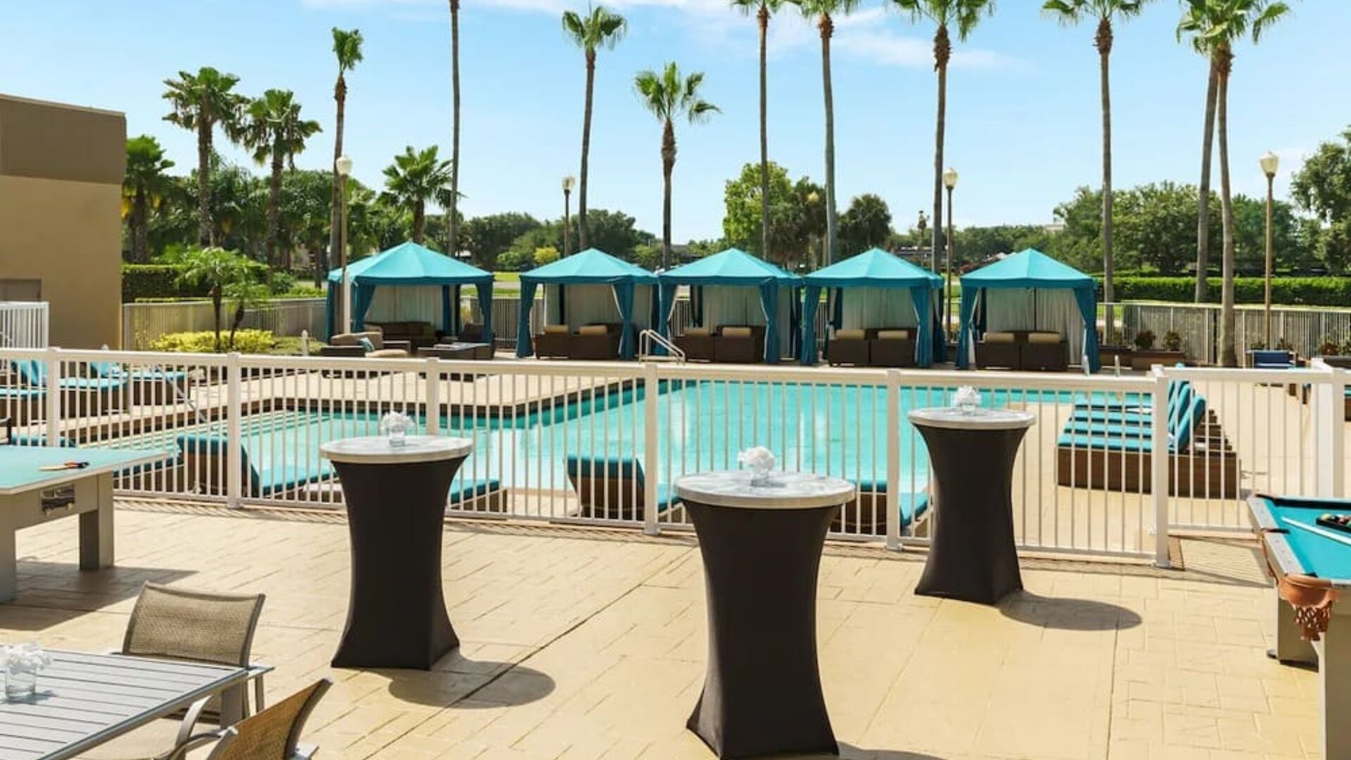 Poolside patio with cocktail tables, cabanas, lounge seating, and recreational games overlooking the pool.