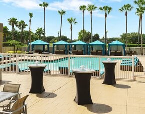 Poolside patio with cocktail tables, cabanas, lounge seating, and recreational games overlooking the pool.