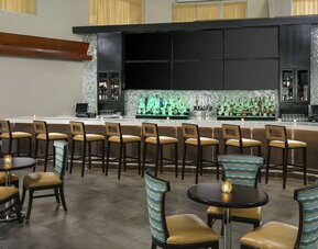 Stylish hotel bar with high-top seating, illuminated back bar, cocktail tables, and lounge-style chairs.