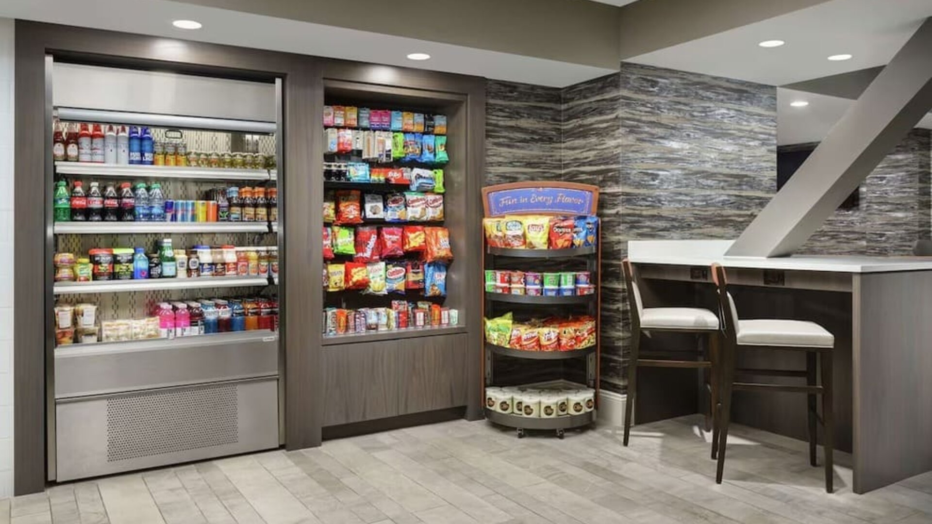 Hotel market offering refrigerated beverages, packaged snacks, pantry items, and casual seating area.