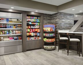 Hotel market offering refrigerated beverages, packaged snacks, pantry items, and casual seating area.