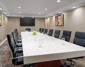 Private meeting room with long conference table, leather executive chairs, and wall-mounted display.