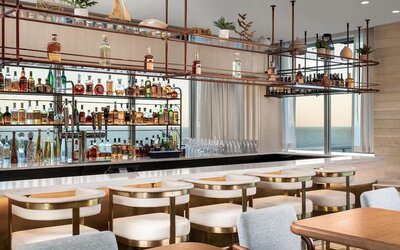 Elegant ocean-view bar with marble countertop, cushioned seating, hanging shelves, and extensive liquor display.