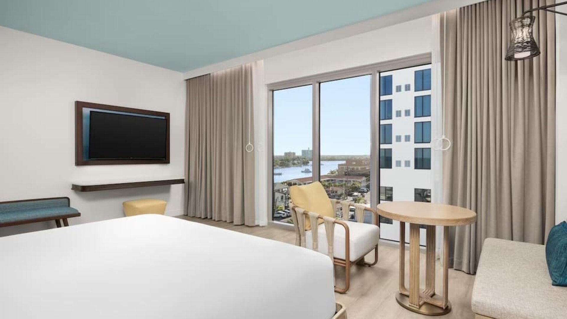 Bright king room with floor-to-ceiling windows, sitting area, round table, and views of the waterfront.