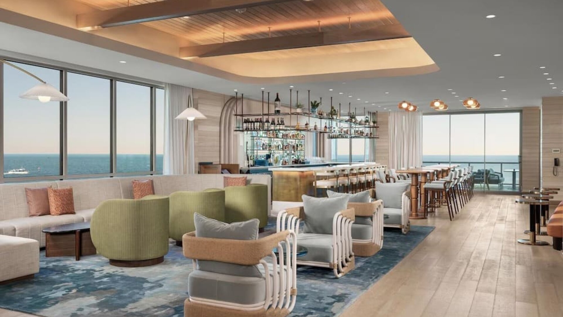 Spacious lounge and bar area with ocean views, plush seating, wood flooring, and contemporary coastal décor.