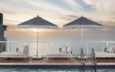 Resort-style pool with shallow tanning ledge, in-water loungers, striped umbrellas, and private cabana seating.