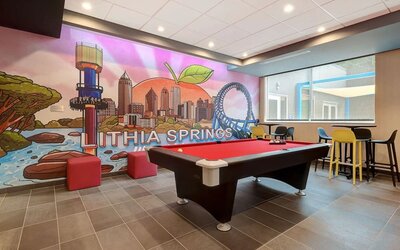 Game room with pool table, colorful Lithia Springs mural, and casual lounge seating at Tru By Hilton Lithia Springs.