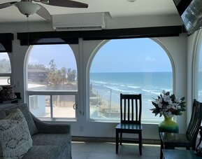 Living area with ocean-view windows, seating, and coastal-inspired interiors at Casa Playa Baja Resort.