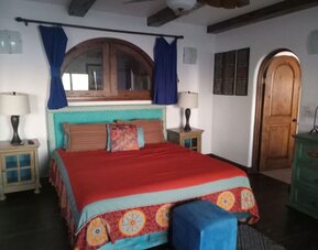 Spacious bedroom with king-size bed, rustic wood accents, exposed beams, and colorful décor at Casa Playa Baja Resort.