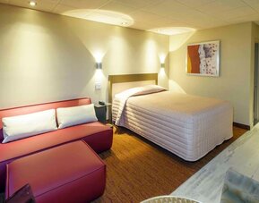 Cozy guest room with queen-size bed, lounge seating and warm contemporary décor at Le Chabrol Hotel Et Suites.