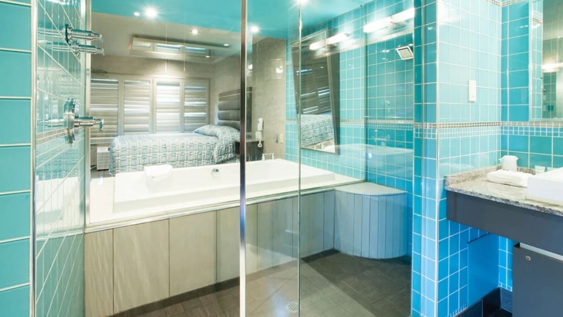 Modern bathroom with glass-enclosed bathtub, turquoise tile accents and vanity at Le Chabrol Hotel Et Suites.