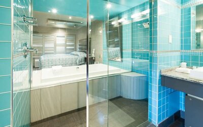 Modern bathroom with glass-enclosed bathtub, turquoise tile accents and vanity at Le Chabrol Hotel Et Suites.