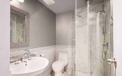 Modern bathroom with walk-in rainfall shower, marble-effect walls and elegant finishes at Le Chabrol Hotel Et Suites.