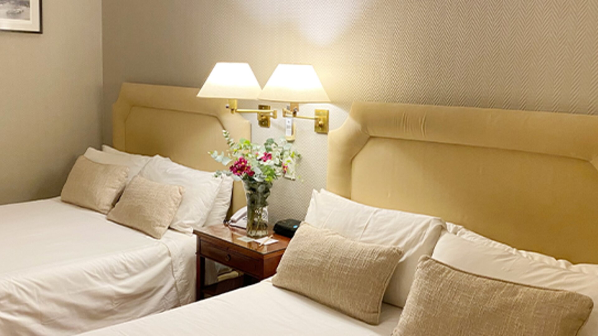 Double guest room with two beds, soft neutral décor, bedside tables, and thoughtful amenities suitable for group or family stays at Hotel Lafayette.