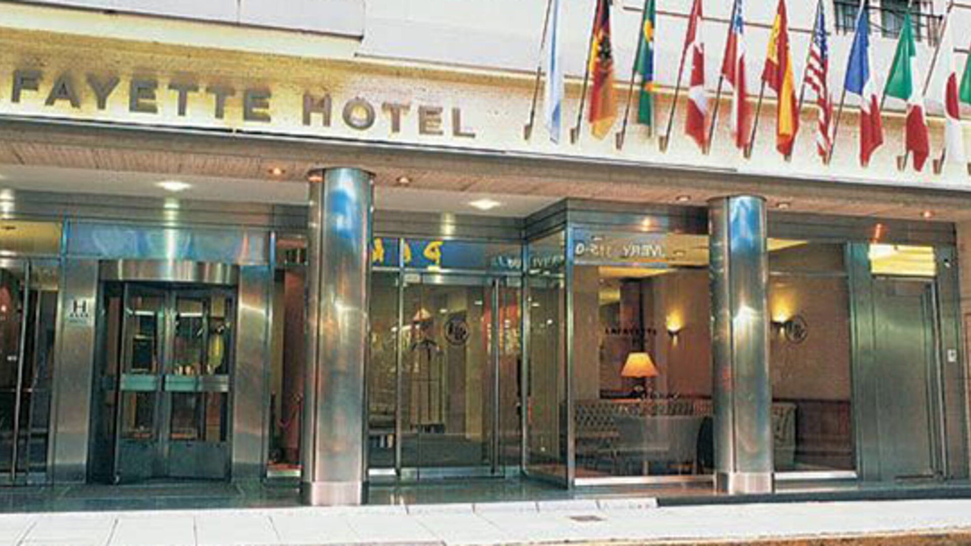 Exterior entrance of the hotel featuring an international flag display, modern glass frontage, and a prime central location at Hotel Lafayette.