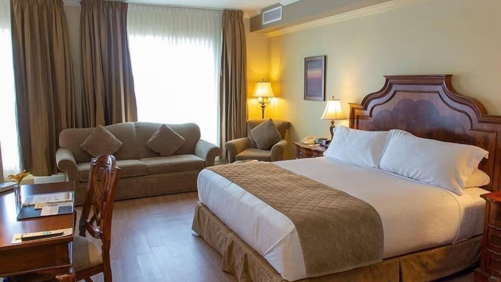 Spacious king guest room with sofa seating, work desk and elegant furnishings at Hotel Brossard.