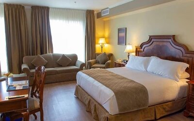 Spacious king guest room with sofa seating, work desk and elegant furnishings at Hotel Brossard.