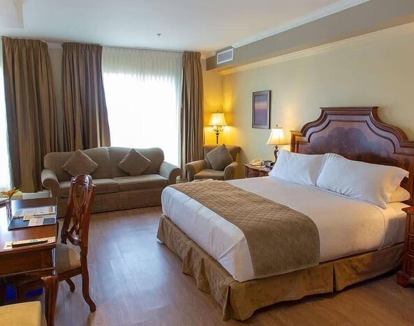 Spacious king guest room with sofa seating, work desk and elegant furnishings at Hotel Brossard.