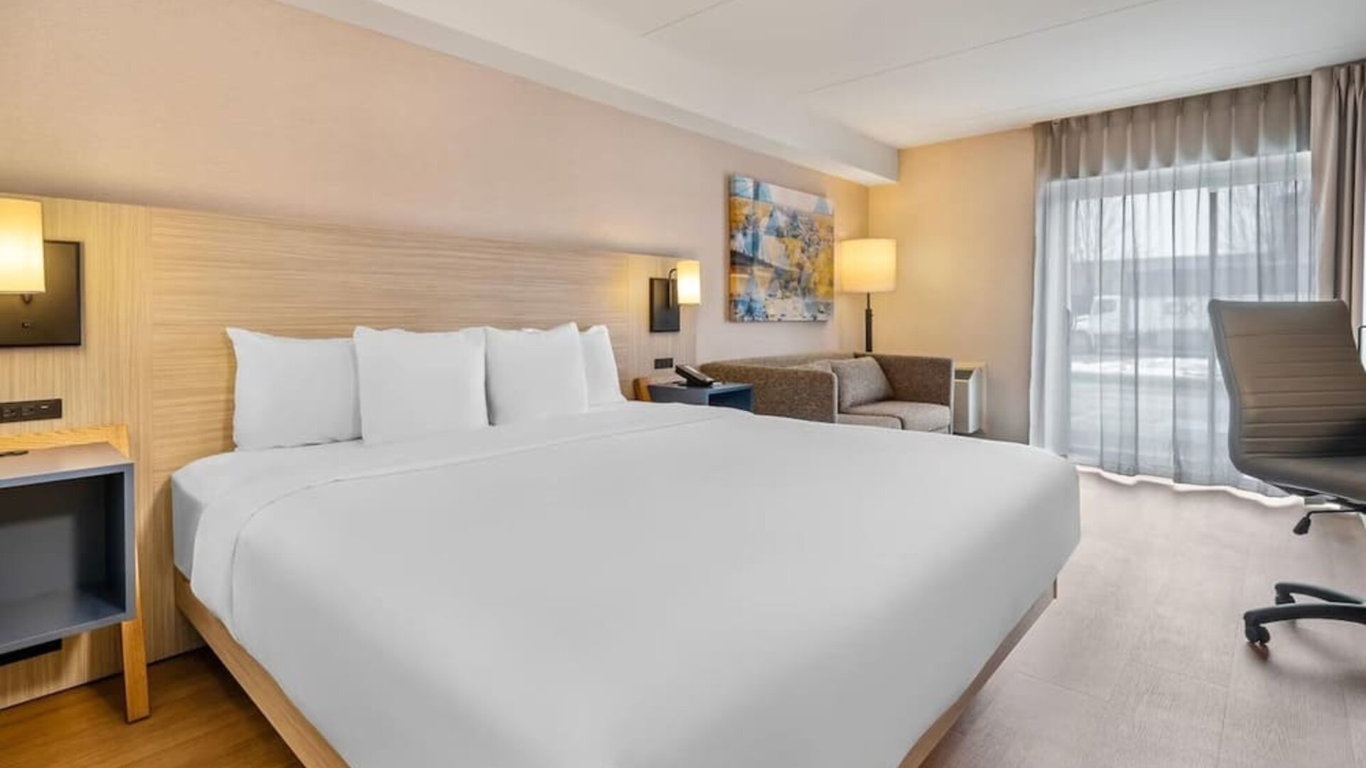 Bright king guest room with comfortable seating, work desk and modern furnishings at Comfort Inn Laval.