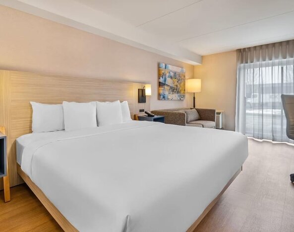 Bright king guest room with comfortable seating, work desk and modern furnishings at Comfort Inn Laval.