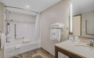 Accessible guest bathroom with bathtub, grab bars, shower seat and illuminated vanity at Days Inn & Suites By Wyndham Lindsay.