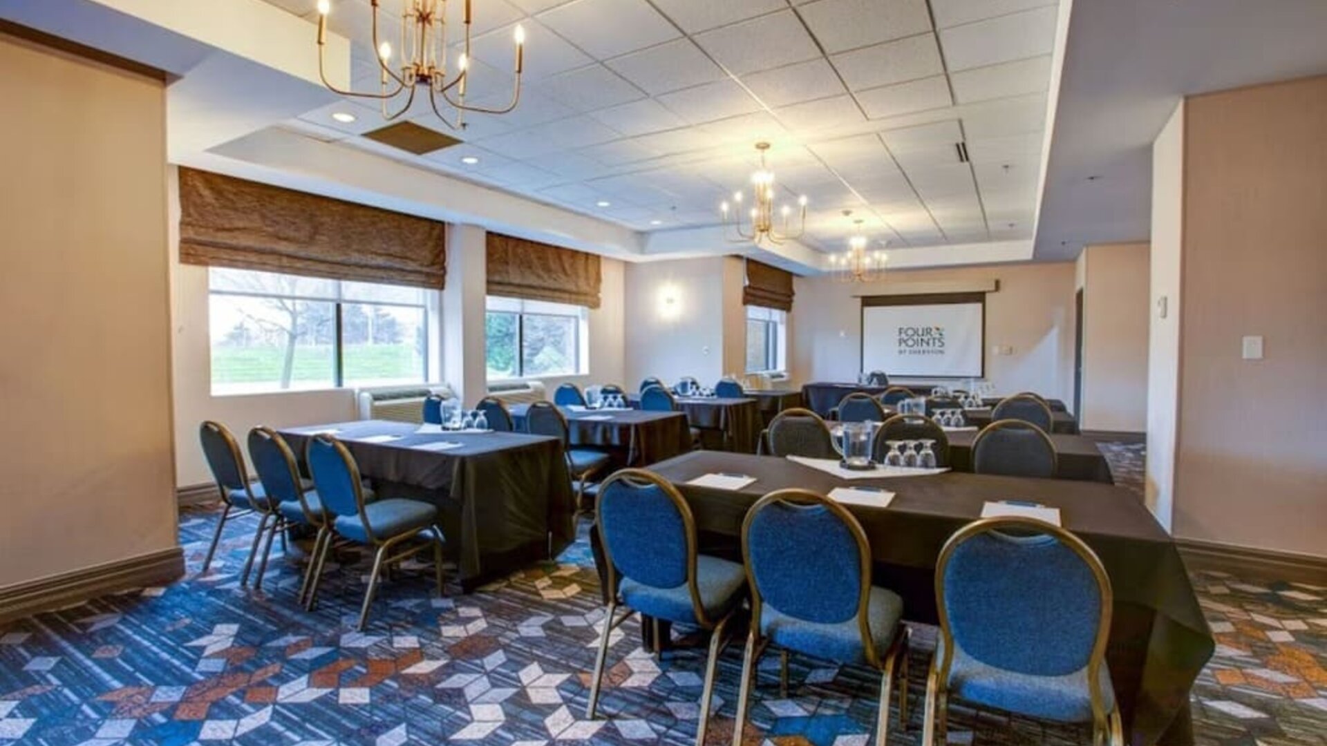 Flexible meeting room with banquet-style seating, presentation screen, and natural light at Four Points by Sheraton St. Catharines Niagara Suites.