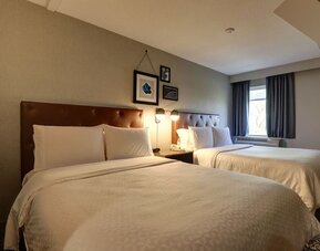 Spacious guest room with two queen beds, comfortable furnishings, and modern décor at Four Points by Sheraton St. Catharines Niagara Suites.