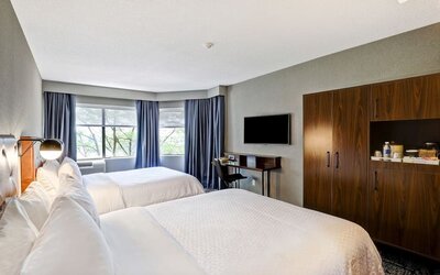 Spacious guest room featuring two plush beds, a large flat-screen TV, and modern furnishings at Four Points by Sheraton St. Catharines Niagara Suites.